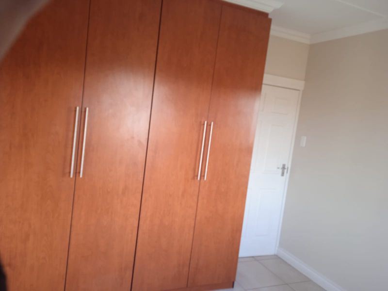 A clean bedroom featuring built-in wooden cupboards, neutral wall paint, and tiled flooring.