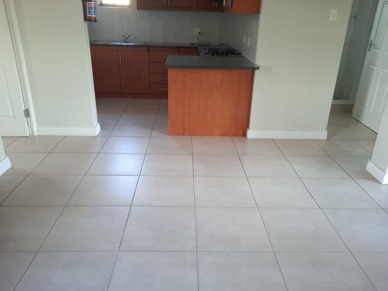 A functional kitchen area featuring laminate cabinetry, dark countertops, a built-in hob, and neutral ceramic floor tiles in an open-plan layout.