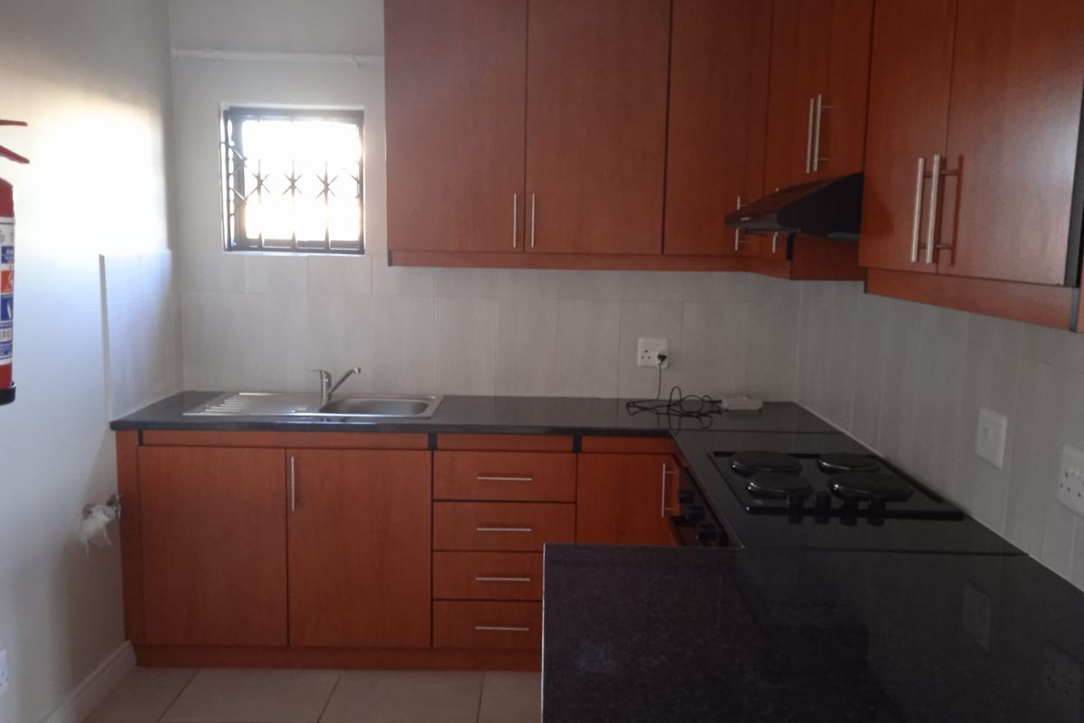 A functional kitchen featuring wood-finish cabinetry, granite countertops, a built-in electric hob with extractor, and tiled splashbacks.