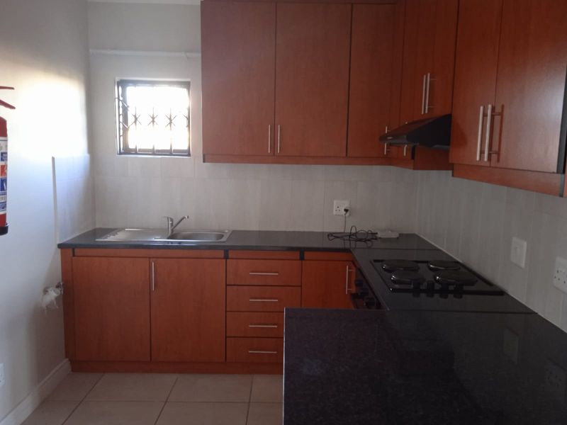 A functional kitchen featuring wood-finish cabinetry, granite countertops, a built-in electric hob with extractor, and tiled splashbacks.