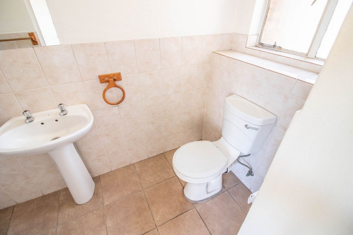 A functional bathroom featuring a pedestal basin, ceramic toilet, and neutral wall and floor tiling, offering a clean and simple layout.