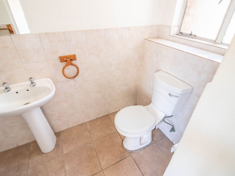 A functional bathroom featuring a pedestal basin, ceramic toilet, and neutral wall and floor tiling, offering a clean and simple layout.