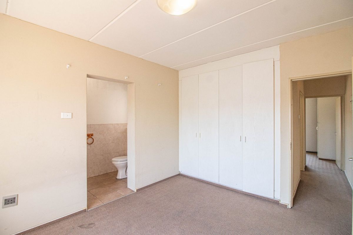 An empty bedroom featuring built-in cupboards, carpeted flooring, and an adjoining en-suite toilet area.