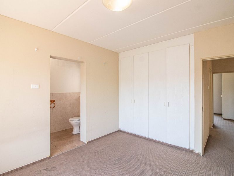 An empty bedroom featuring built-in cupboards, carpeted flooring, and an adjoining en-suite toilet area.