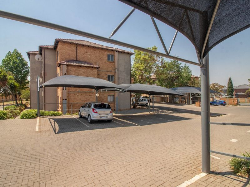 Exterior view of the townhouse complex featuring paved parking areas with installed shade cloth carports and multi-story brick residential buildings.
