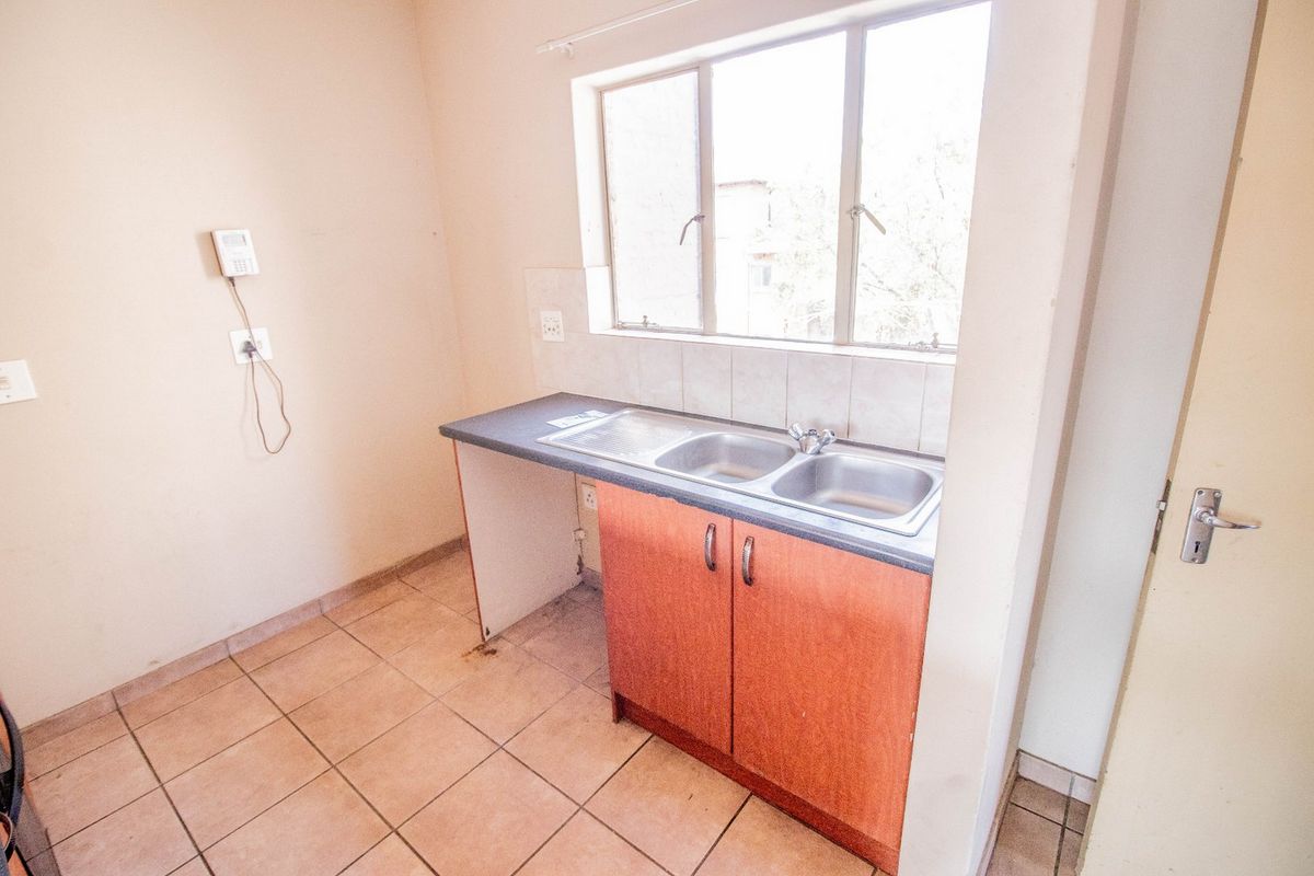 A compact kitchen area featuring a double bowl stainless steel sink, laminate countertop, tiled splashback, and built-in base cabinetry with tiled flooring.