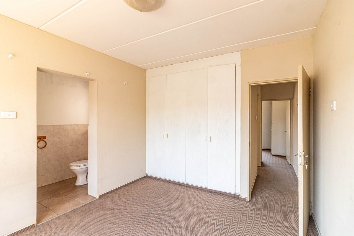 An empty bedroom featuring built-in cupboards, carpeted flooring, and an attached en-suite toilet area with tiled finishes.