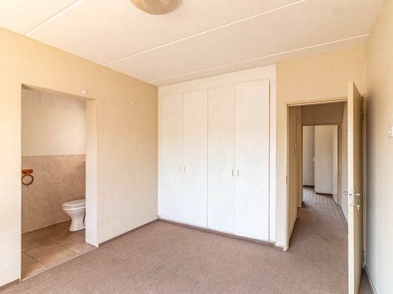An empty bedroom featuring built-in cupboards, carpeted flooring, and an attached en-suite toilet area with tiled finishes.
