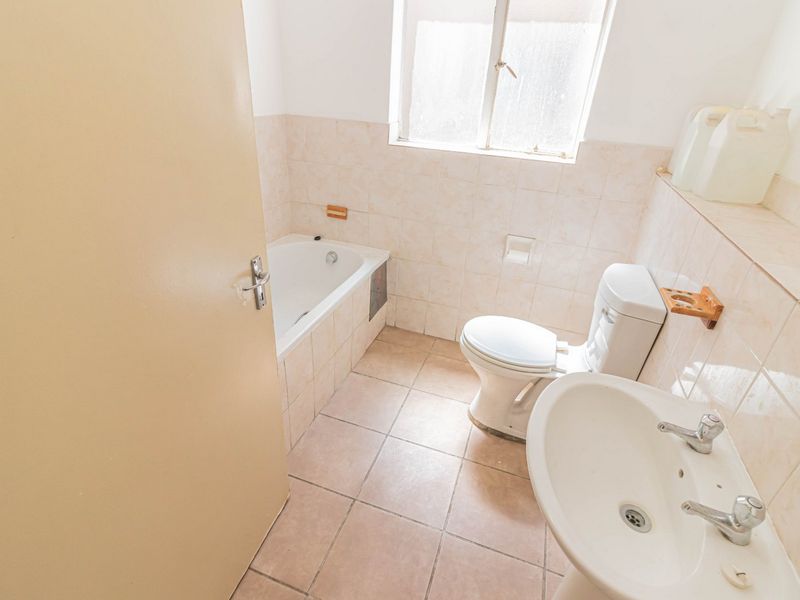 A dated bathroom featuring a bathtub, pedestal basin, and toilet with neutral wall and floor tiling.