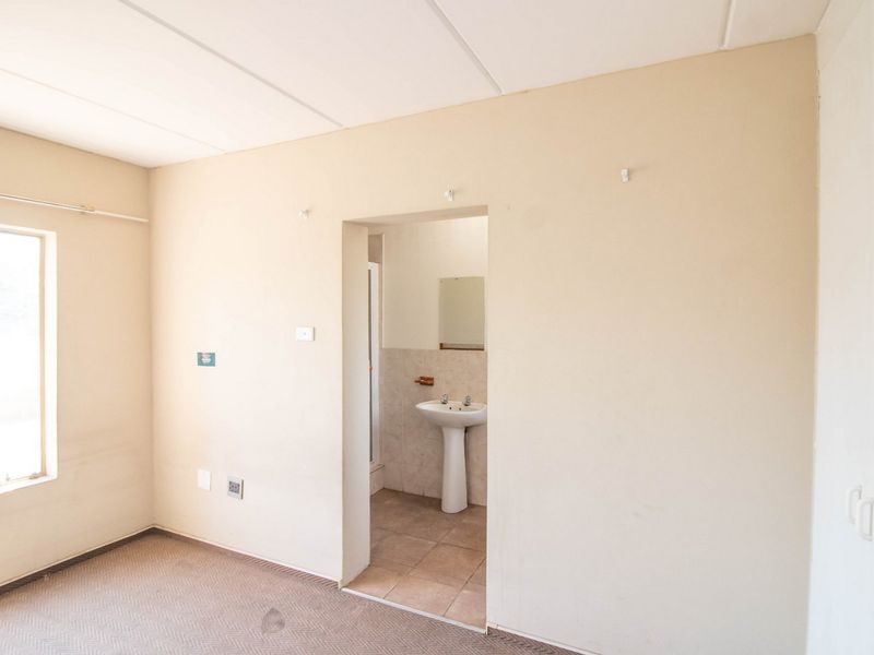 An empty bedroom featuring carpeted flooring and an adjoining en-suite bathroom with a pedestal basin and tiled flooring.