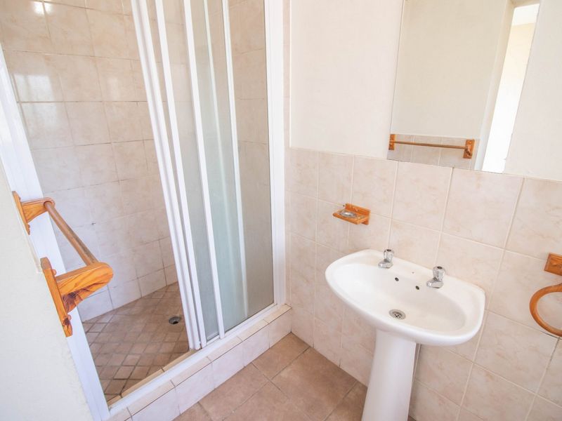 A functional bathroom featuring a pedestal basin, a shower enclosure with sliding doors, and neutral wall and floor tiling.