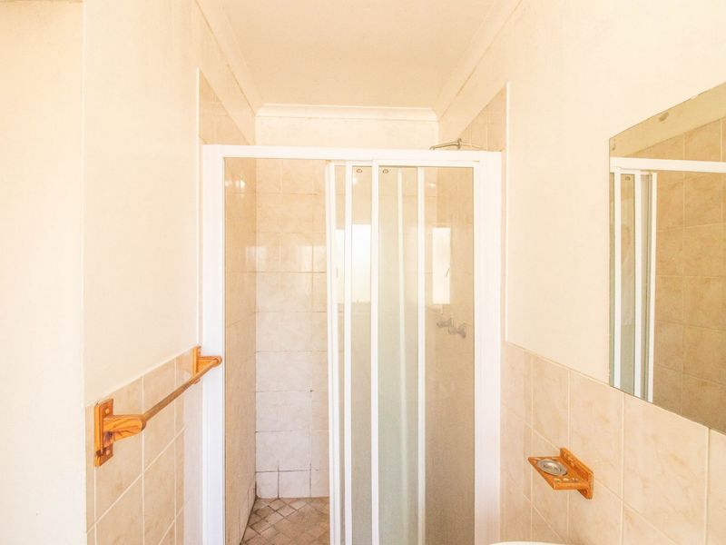 A functional bathroom featuring a shower enclosure with a sliding door, tiled walls, and a wall-mounted mirror.