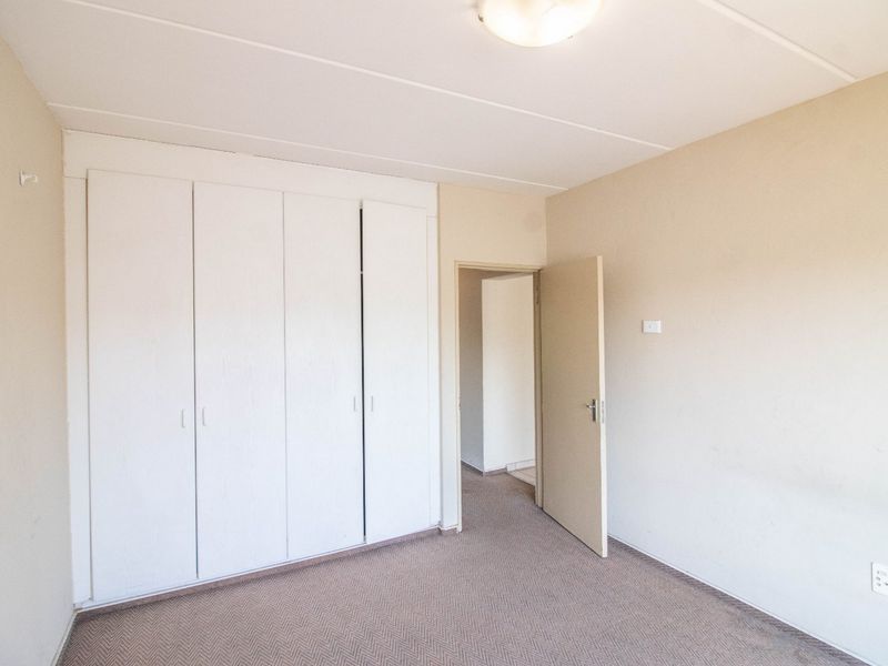 A clean, empty bedroom featuring neutral walls, carpeted flooring, and built-in cupboards, offering a blank canvas for personalization.