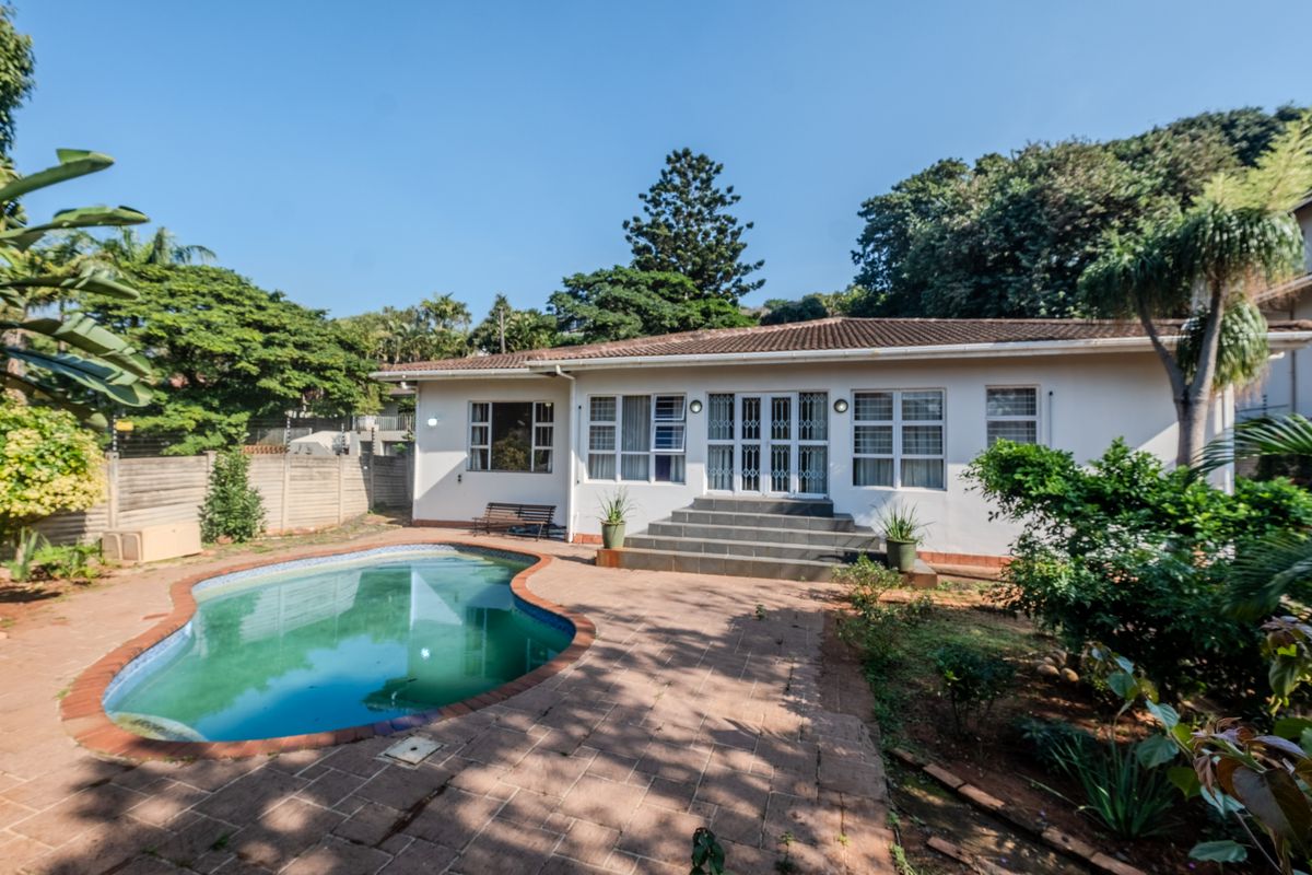 Rear view of the house featuring a swimming pool, paved patio area, and direct access to the garden through double doors.