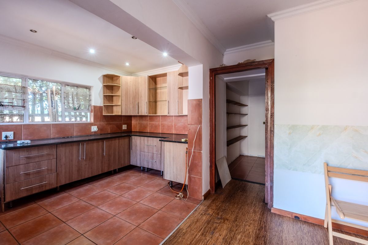 A functional kitchen featuring laminate cabinetry, granite countertops, and tiled flooring, with an adjacent walk-in pantry and direct access to the living area.