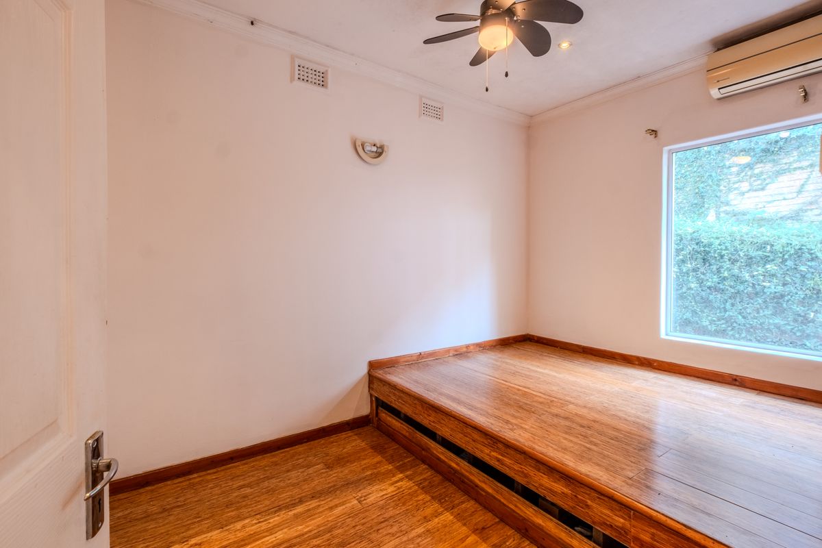 A bright bedroom featuring timber flooring, a built-in timber platform, a ceiling fan, and a wall-mounted split system air conditioner.