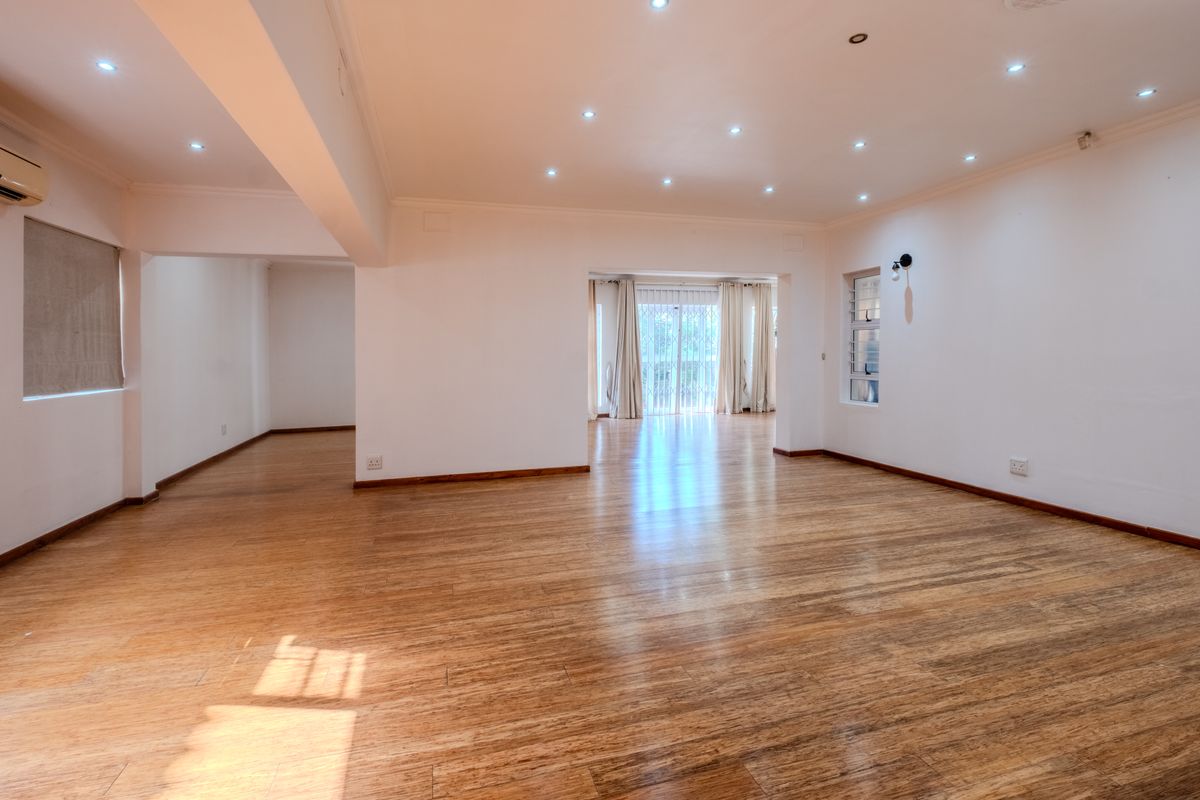 Spacious, open-plan living area featuring warm laminate flooring, recessed downlighting, and large sliding doors providing natural light and access to the exterior.