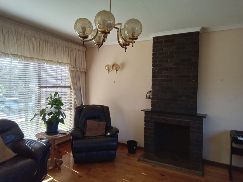 A living room featuring a prominent dark brick fireplace, polished hardwood flooring, and classic lighting fixtures, offering a cozy and traditional atmosphere.