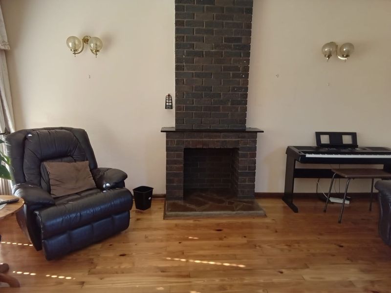 Living room featuring a prominent brick fireplace, polished hardwood flooring, and wall-mounted lighting fixtures.