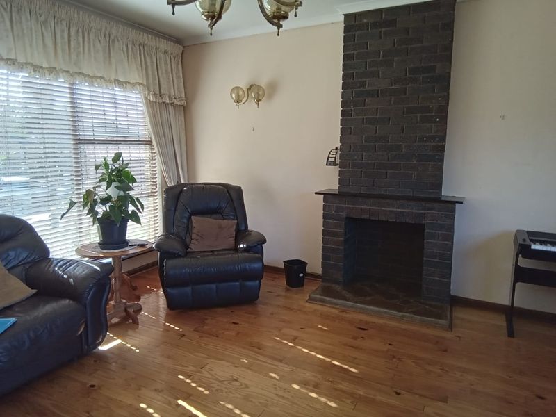 A living room featuring a prominent dark brick fireplace, hardwood flooring, and natural light through venetian blinds.