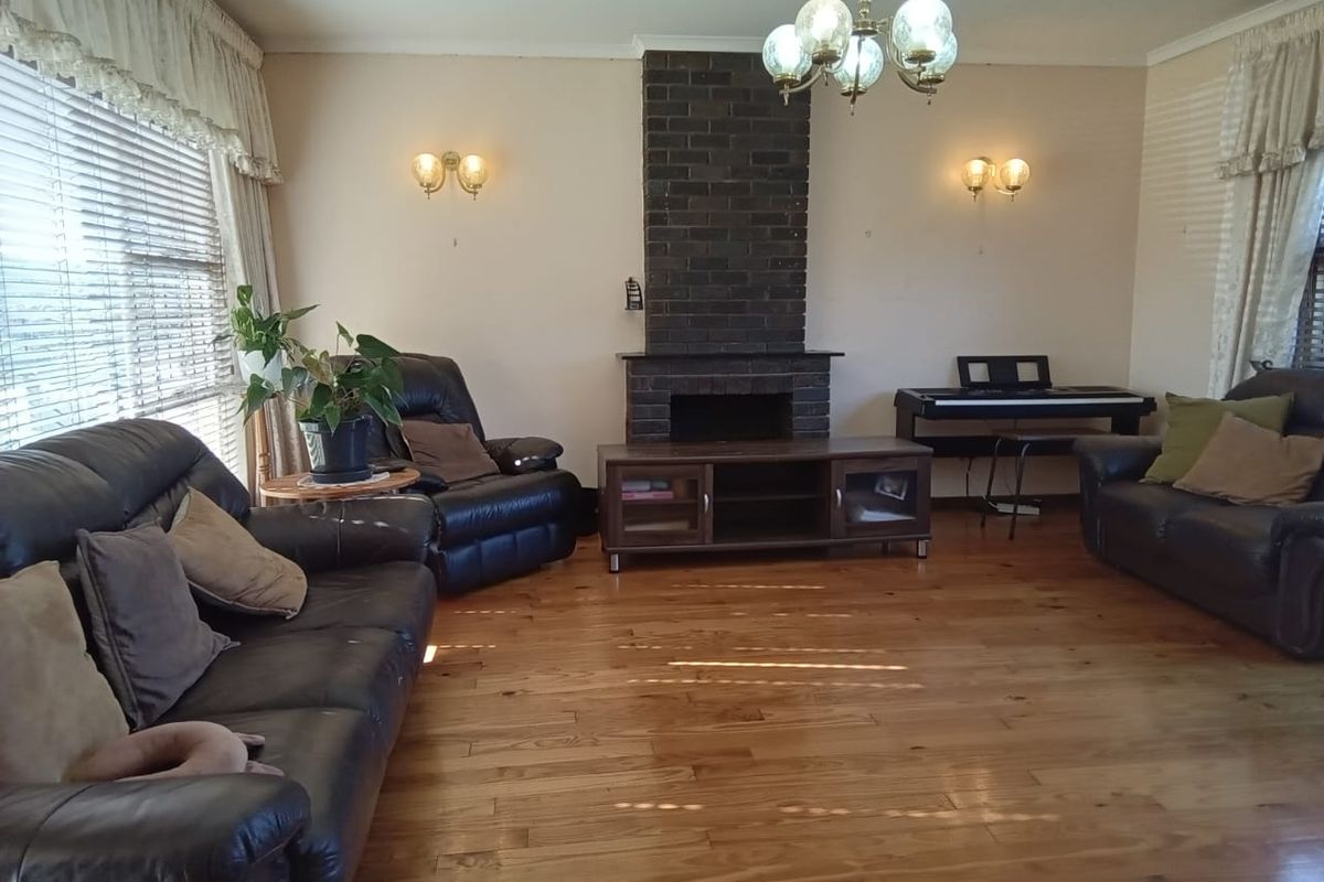 Spacious living room featuring a prominent brick fireplace, warm hardwood flooring, and classic wall sconce lighting.