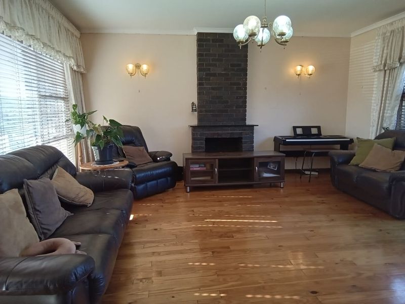 Spacious living room featuring a prominent brick fireplace, warm hardwood flooring, and classic wall sconce lighting.