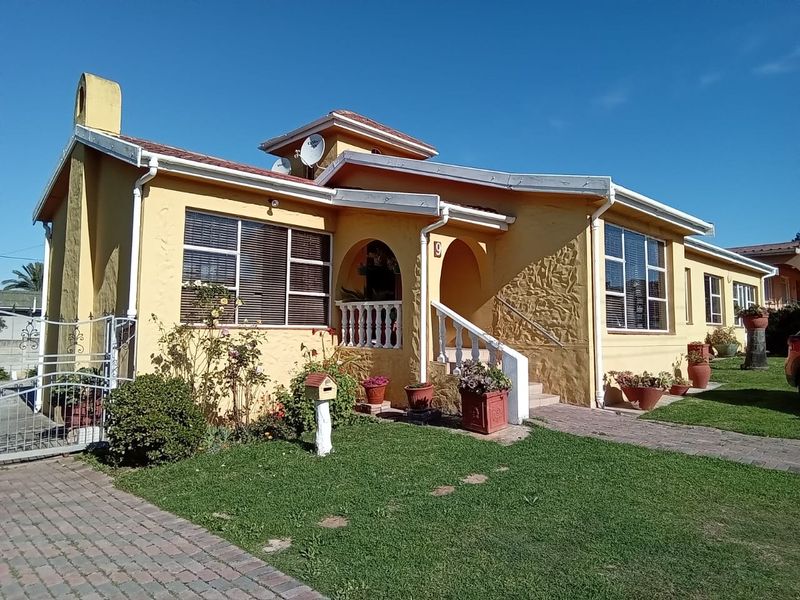 Front elevation of a single-story house featuring a yellow stucco facade, arched entrance with balustrade, and a paved driveway.