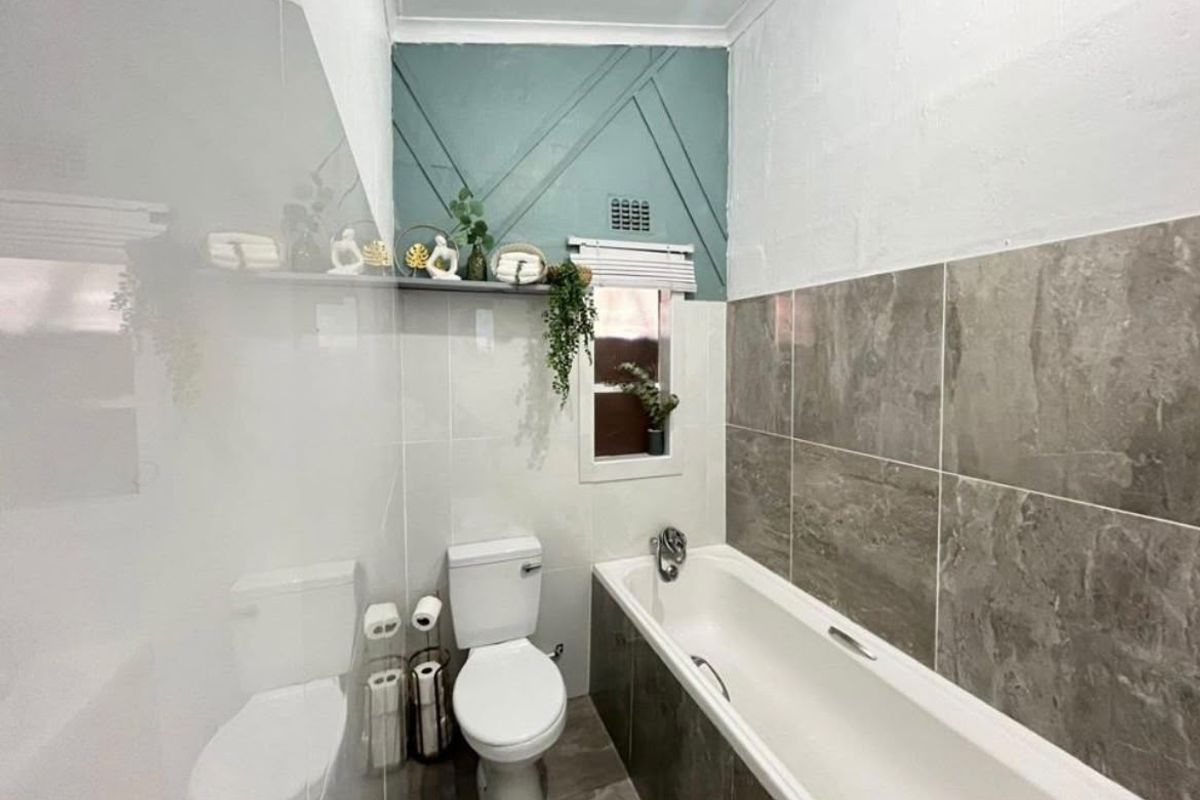 A modern bathroom featuring a bathtub, toilet, and stylish wall tiling with decorative accent paneling.