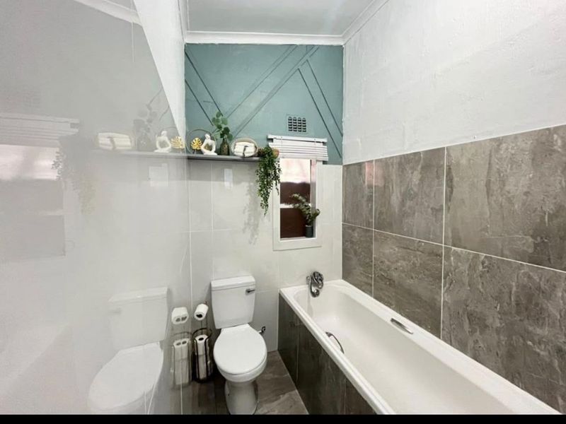 A modern bathroom featuring a bathtub, toilet, and stylish wall tiling with decorative accent paneling.