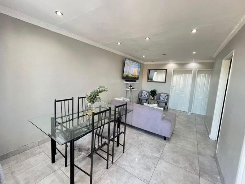 An open-plan living and dining area featuring neutral wall tones, tiled flooring, and recessed downlighting throughout the space.