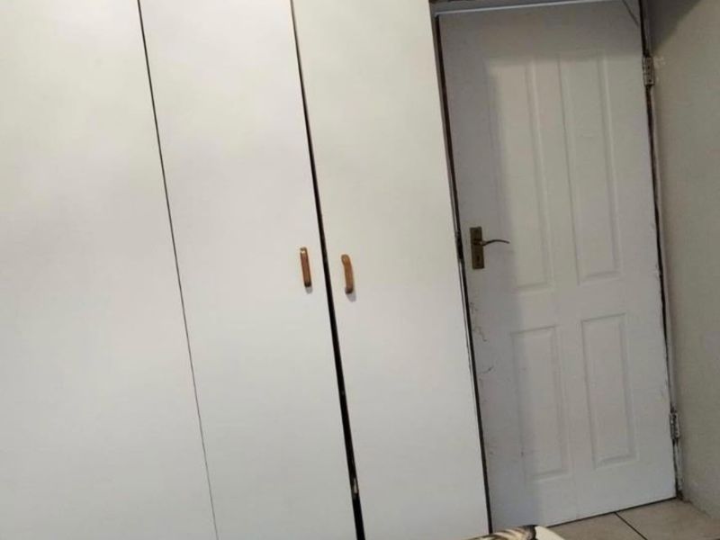 Bedroom featuring white built-in cupboards with overhead storage and tiled flooring.
