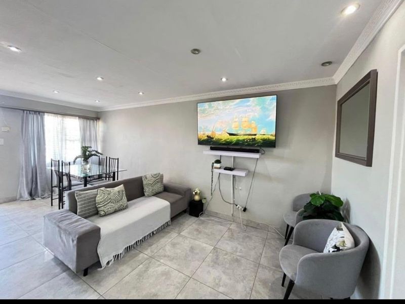 Open-plan living and dining area featuring neutral tiled flooring, recessed downlighting, and decorative ceiling cornicing.