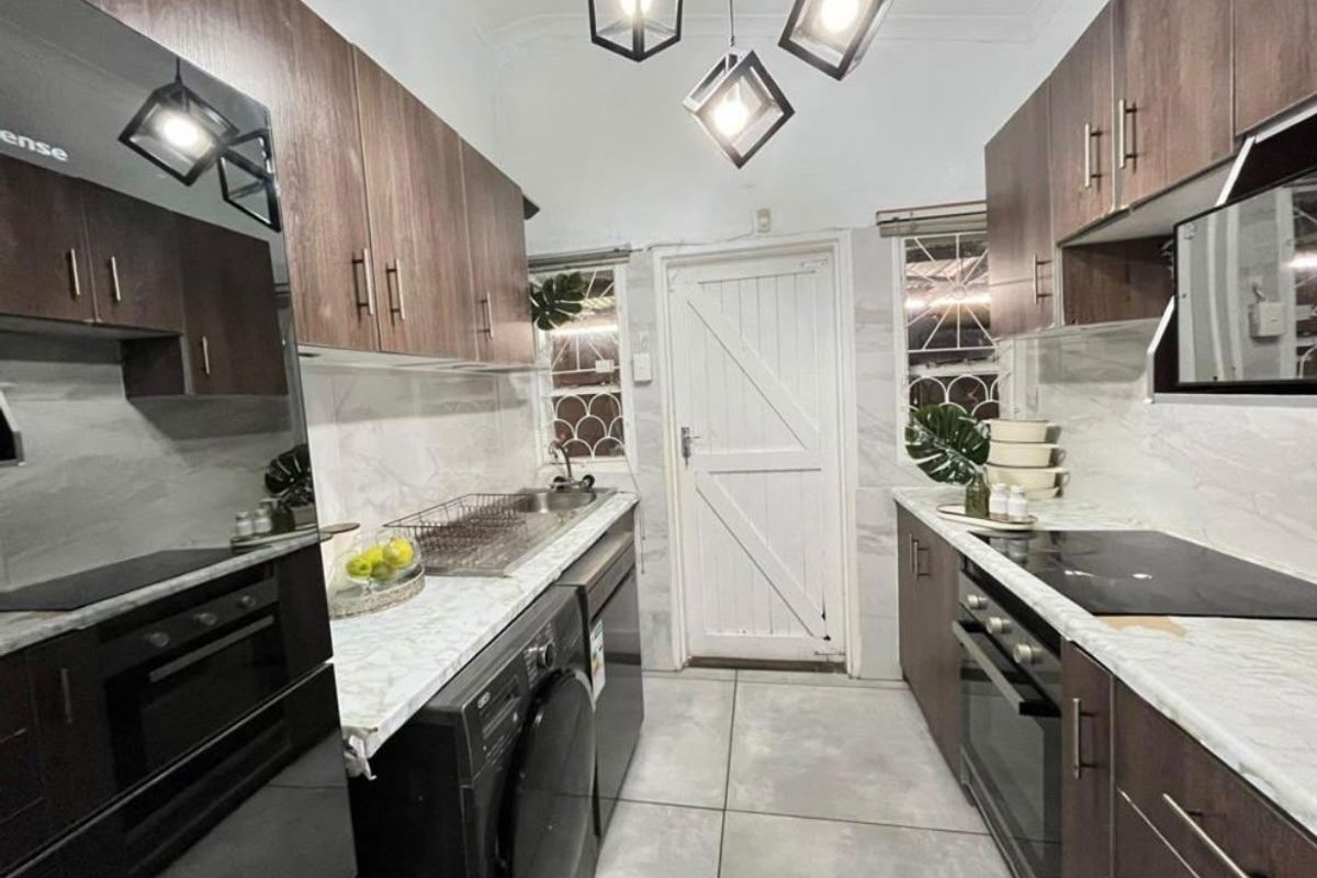 Modern galley-style kitchen featuring dark wood cabinetry, marble-look countertops, integrated appliances, and contemporary pendant lighting with tiled flooring.