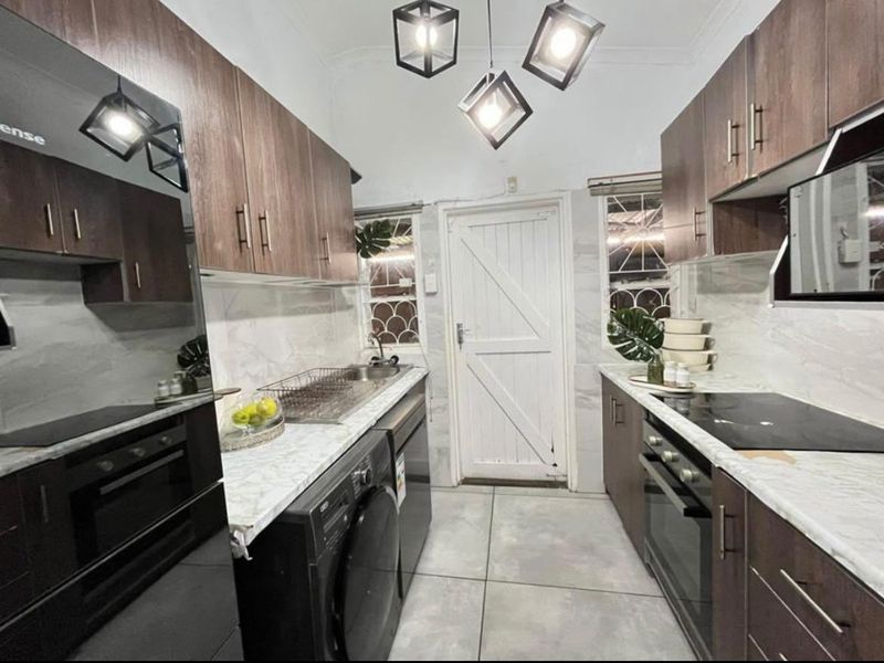 Modern galley-style kitchen featuring dark wood cabinetry, marble-look countertops, integrated appliances, and contemporary pendant lighting with tiled flooring.
