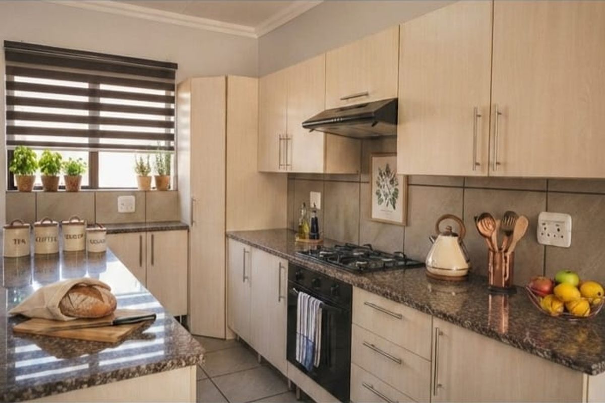 Modern kitchen featuring light wood cabinetry, granite countertops, built-in gas hob, oven, and extractor fan with neutral tiled finishes.
