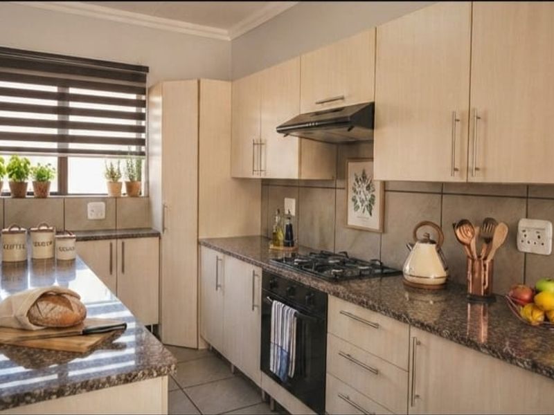 Modern kitchen featuring light wood cabinetry, granite countertops, built-in gas hob, oven, and extractor fan with neutral tiled finishes.