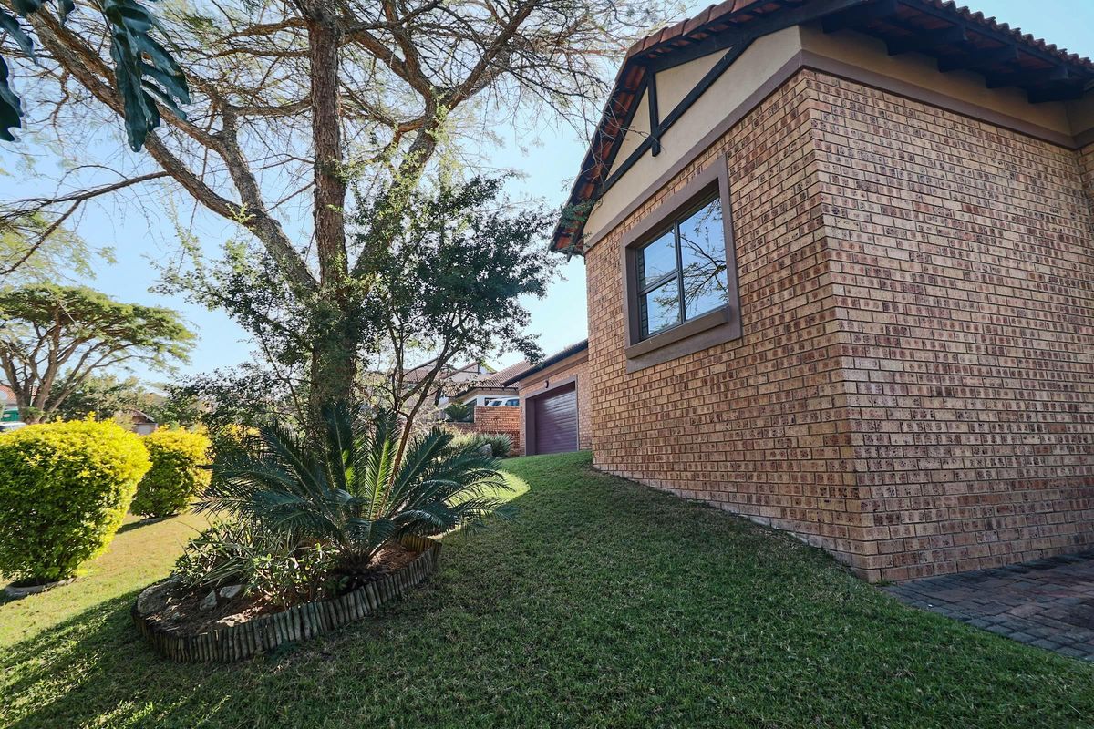 A well-maintained face brick exterior featuring a landscaped garden, mature trees, and a secure garage entrance.