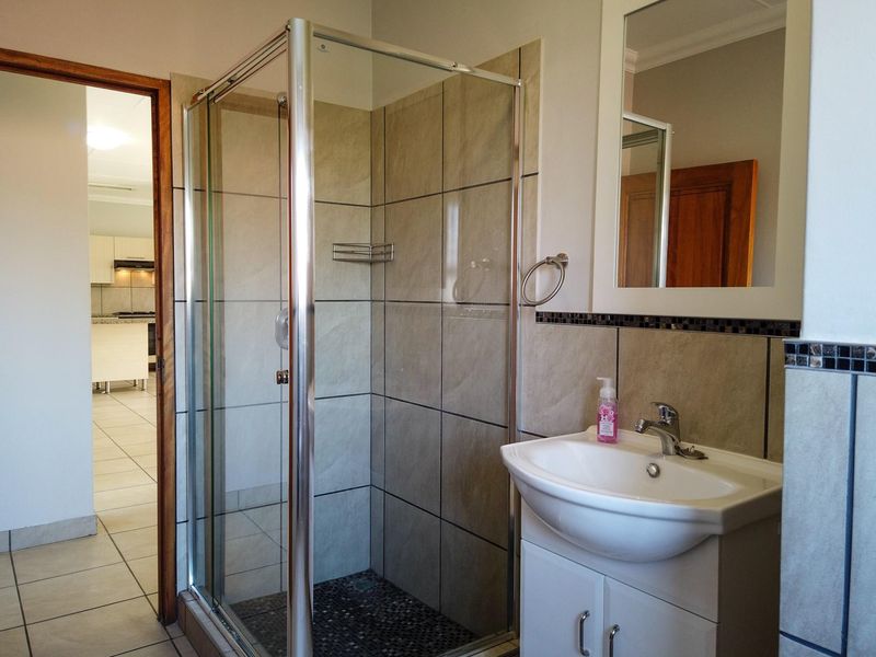 A functional bathroom featuring a glass-enclosed shower with pebble flooring, a vanity basin with storage, and a wall-mounted mirror.