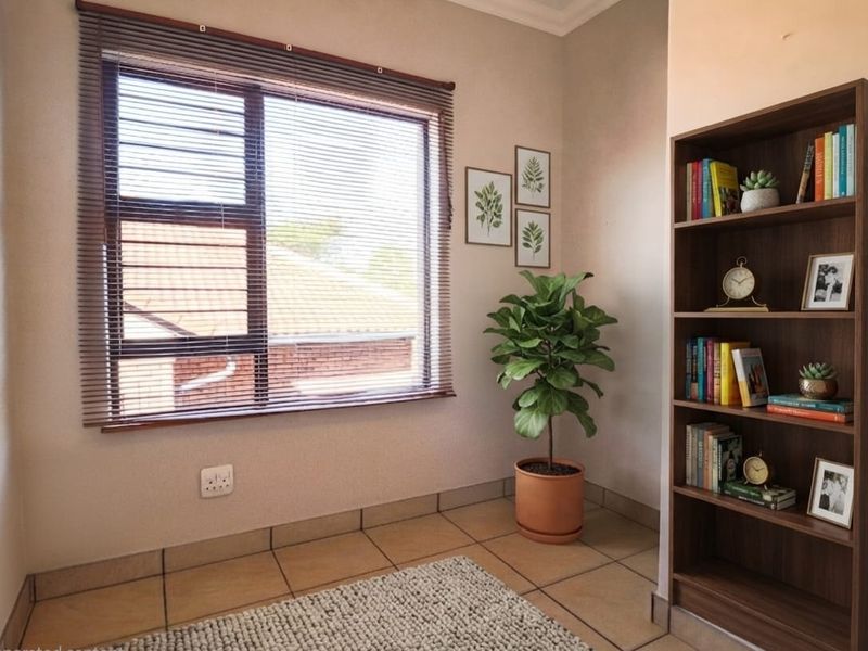 A bright living area featuring neutral tiled flooring, a large window with venetian blinds, and a built-in wall nook.