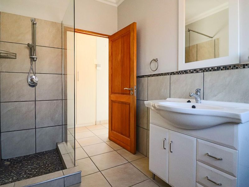 A clean, modern bathroom featuring a glass-enclosed shower, a vanity unit with a basin, and neutral wall and floor tiling.