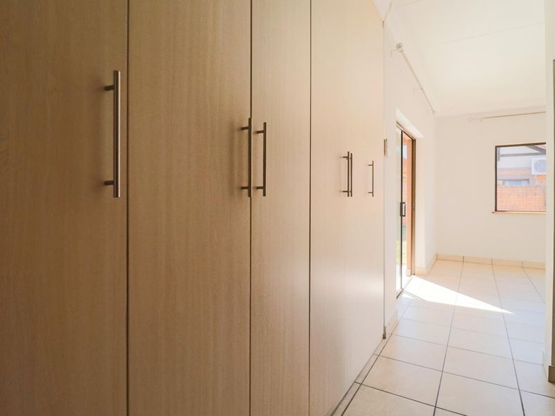 A bright, empty hallway featuring extensive built-in light wood cabinetry, tiled flooring, and access to an outdoor area via a sliding glass door.