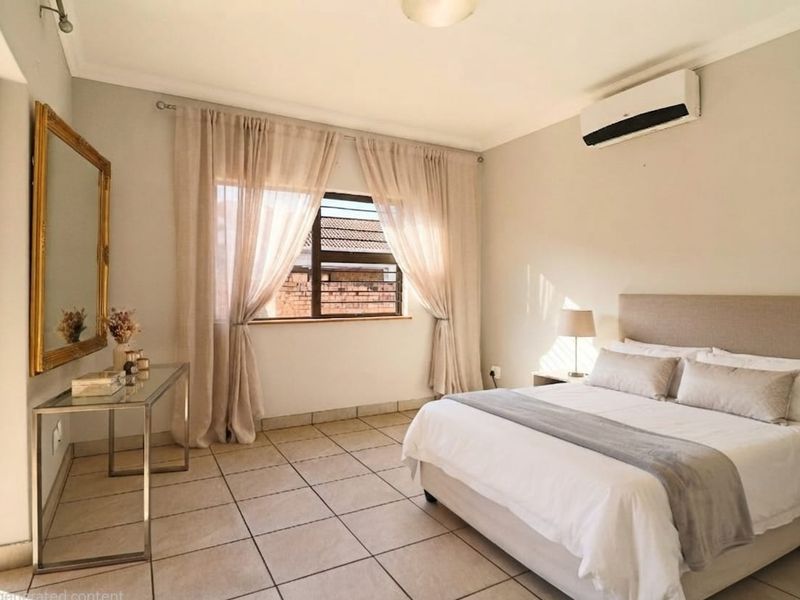A well-lit bedroom featuring neutral tiled flooring, a wall-mounted split-system air conditioner, and large windows with security bars.
