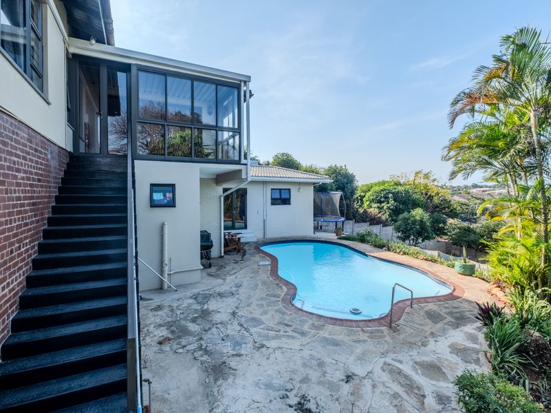 Outdoor pool area featuring a kidney-shaped swimming pool, stone paving, and an external staircase leading to an enclosed upper balcony.