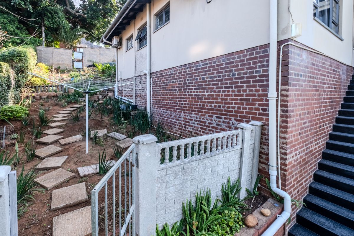 Rear exterior view showing a brick facade, concrete staircase, and a terraced garden with a stepped path and boundary wall.