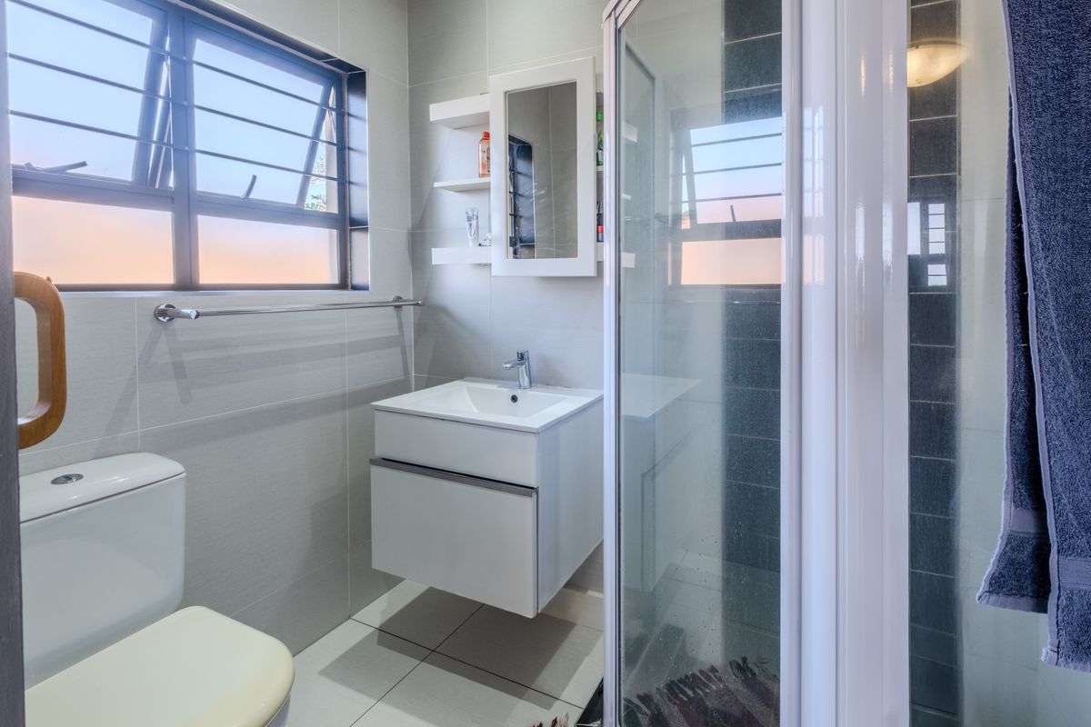 A modern, well-maintained bathroom featuring a wall-mounted vanity, a glass shower enclosure, and neutral floor-to-ceiling tiling.