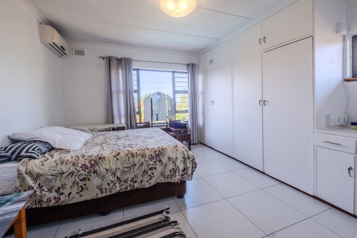 A functional bedroom featuring tiled flooring, extensive built-in cupboard storage, and a wall-mounted split-system air conditioning unit.