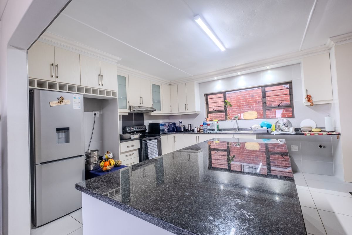 A well-maintained kitchen featuring granite countertops, a central island, ample built-in cabinetry, and tiled flooring, offering a functional and clean workspace.