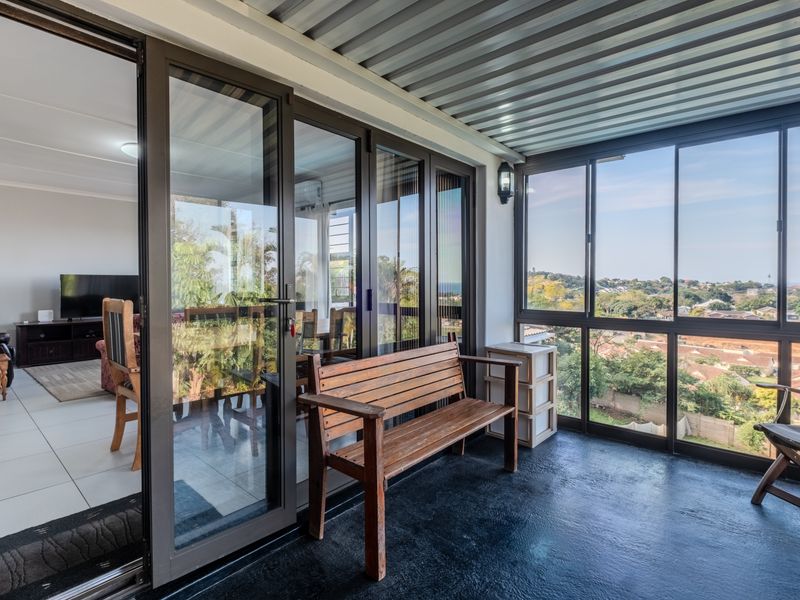 A covered patio area featuring large glass windows, sliding doors leading to the interior, and a corrugated metal ceiling with scenic neighborhood views.