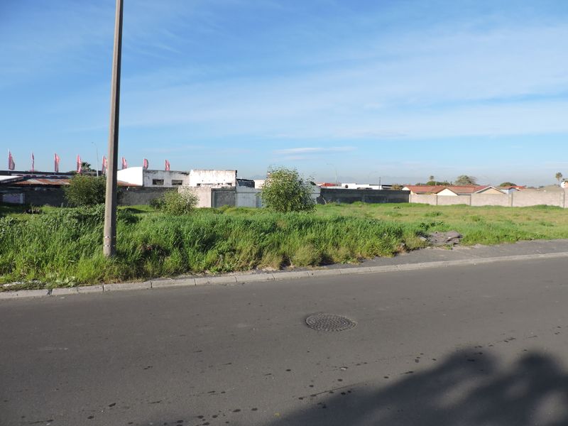 A vacant residential plot featuring a level grassed surface, bordered by a perimeter wall and accessible from a paved street with utility infrastructure.