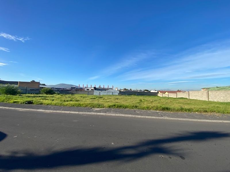 A street-level view of a vacant residential plot featuring a perimeter boundary wall and direct access from an asphalt road.